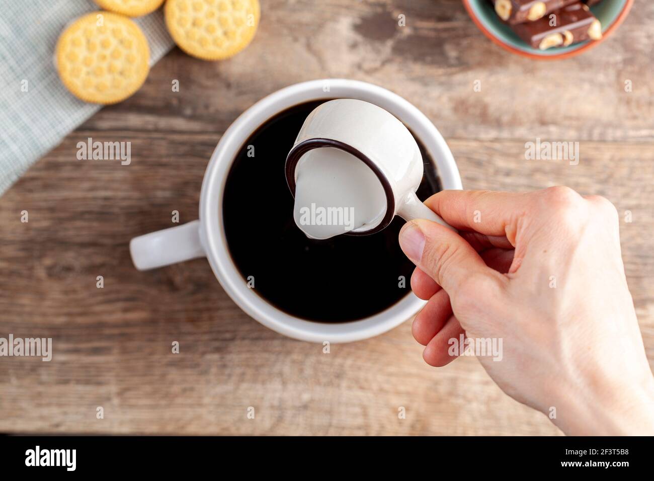 a tea time or coffee time concept with sandwich cookies, bars of chocolate aesthetic ceramic mug and plates as well as a mini creamer pitcher on woode Stock Photo