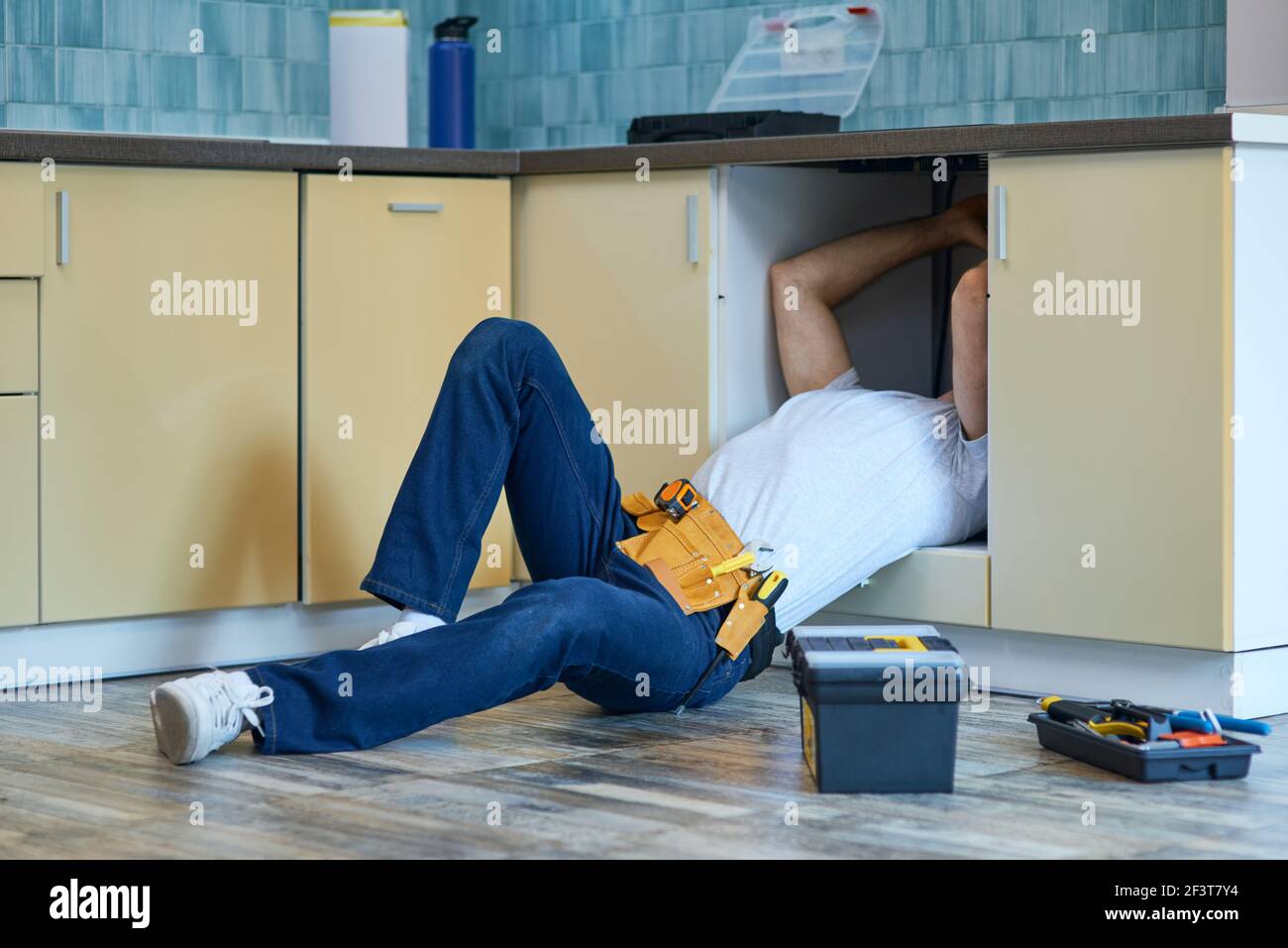 Efficient work. Professional plumber wearing tool belt fixing sink pipe indoors Stock Photo