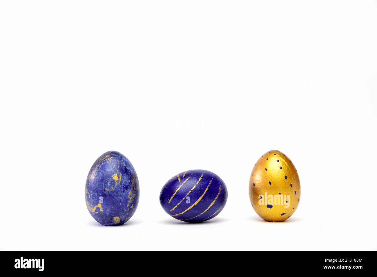 Three easter eggs trendy colored classic blue, white and golden decorated on white table. Happy Easter card with copy space for text. Minimal style Stock Photo