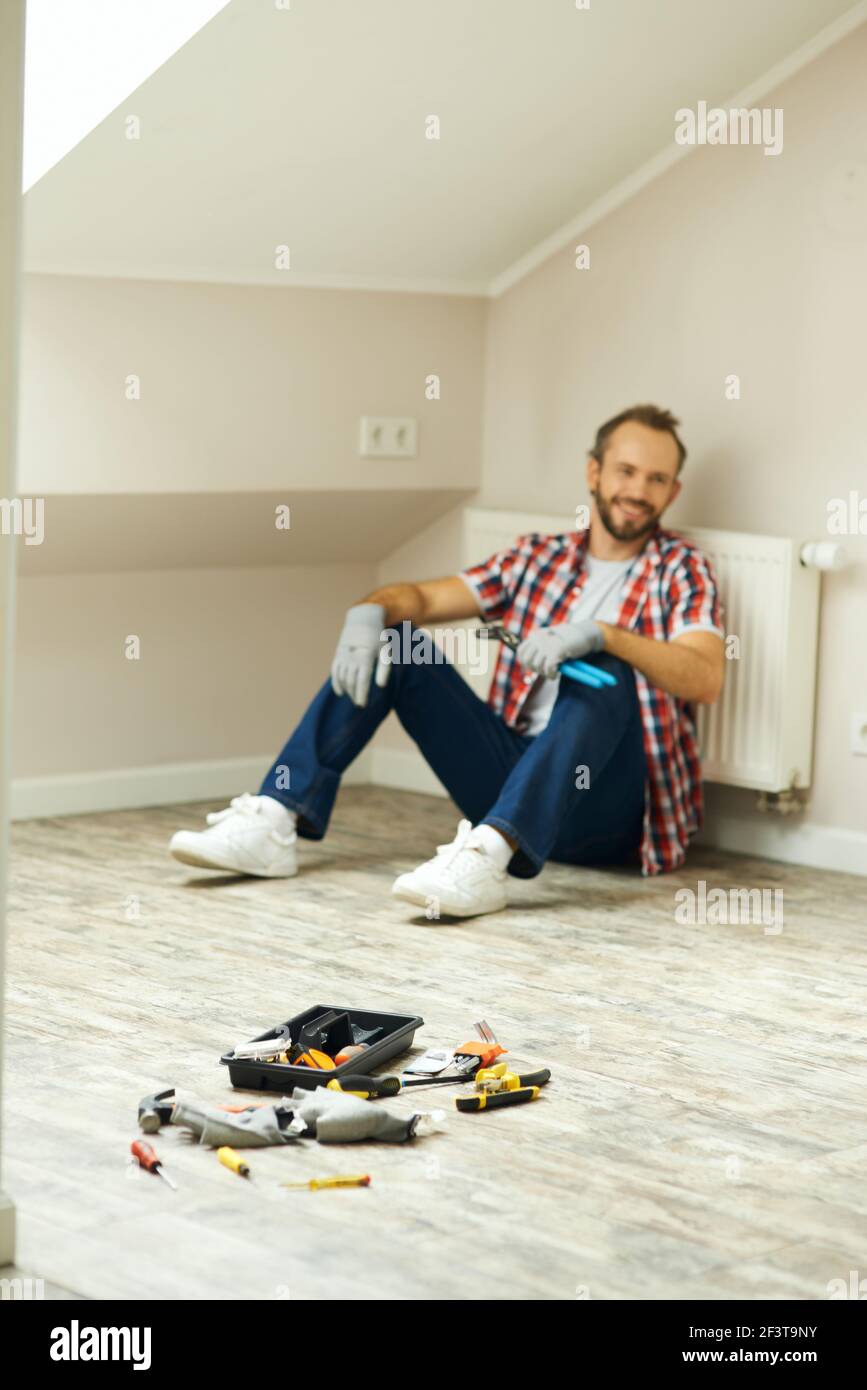 Blurred shot of cheerful handyman using pipe wrench for repairing radiator battery in the room. Home repair hand tools on laminate flooring Stock Photo
