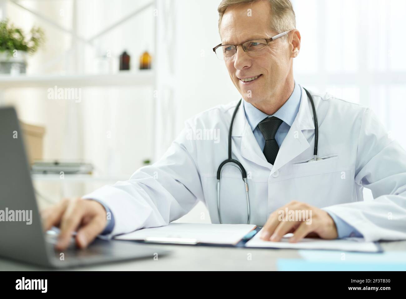 Cheerful doctor using modern notebook in clinic Stock Photo