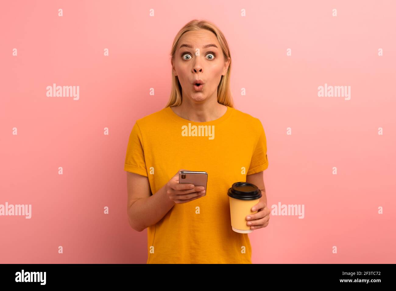 Blonde cute girl types a message with her smartphone. Happy and surprised expression face. Pink background Stock Photo