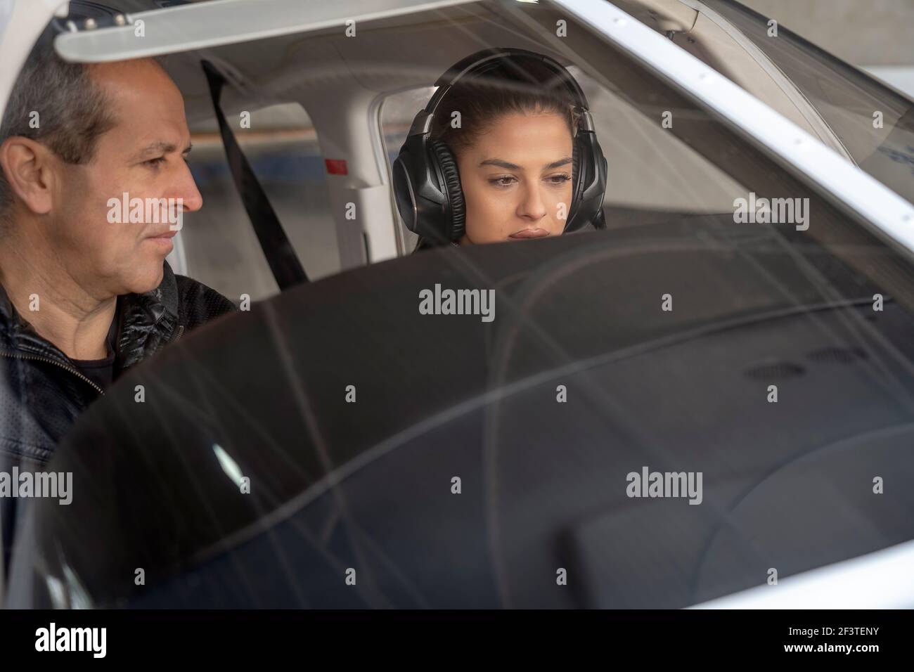 Portrait of attractive young woman trainee pilot with headset preparing to fly. She is sitting next to flight instructor and looking at dashboard. Stock Photo