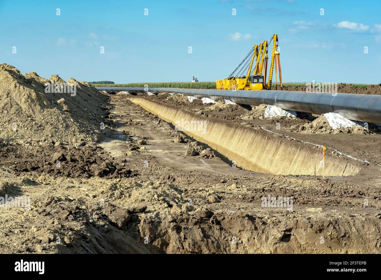 Heavy Machinery and Gas Pipeline Construction Site. Pipes are Laid on Top of Supportive Sandbags Beside Trench and Welded Together. Stock Photo