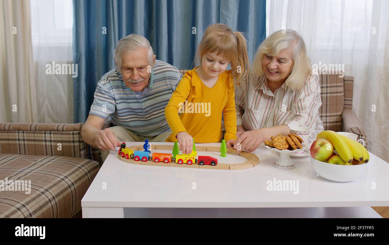 Mature couple grandmother, grandfather with child girl grandkid riding toy train on railroad at home Stock Photo