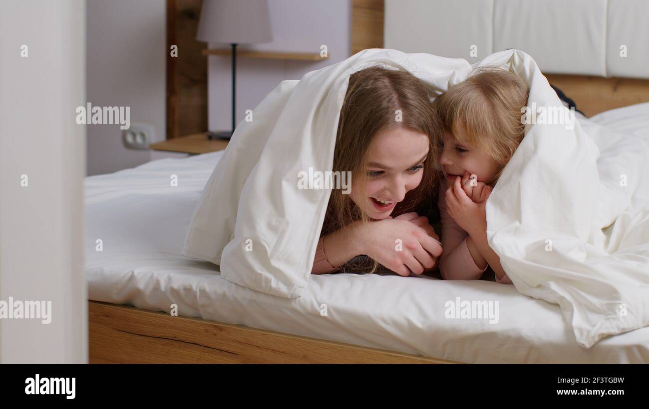 Happy family of mother with daughter lying on bed under duvet blanket