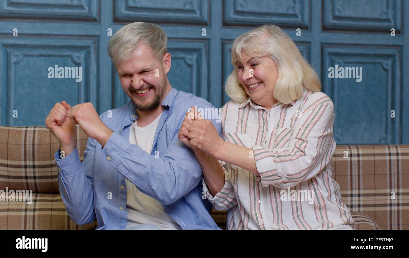 Generations family of senior mother and handsome adult son or grandson dancing together, laughing Stock Photo