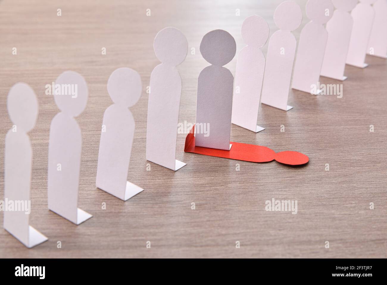 Concept of social exclusion with many little white paper men lined up and one stepping on a different one on wooden base elevated view. Stock Photo