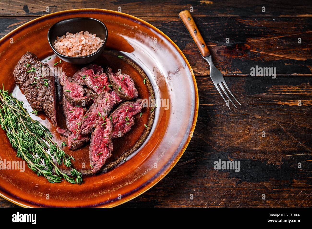 Medium rare Sliced grilled Onglet Hanging Tender meat beef steak on a plate. Dark wooden background. Top view. Copy space Stock Photo