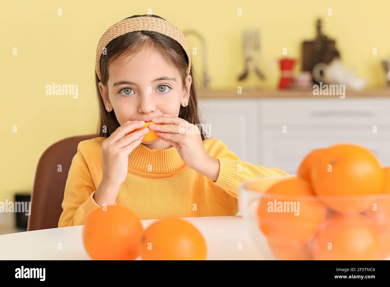 Cute little girl eating orange in kitchen Stock Photo Alamy