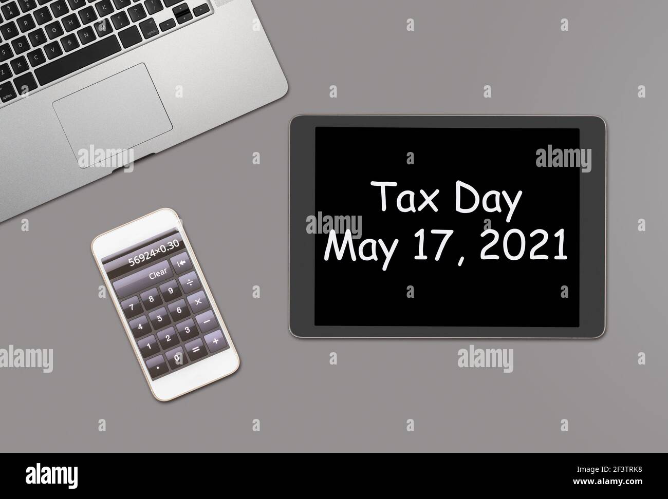 Overhead clean grey desk for laptop, smartphone and tablet computer with message for tax day 2021 as May 17 Stock Photo