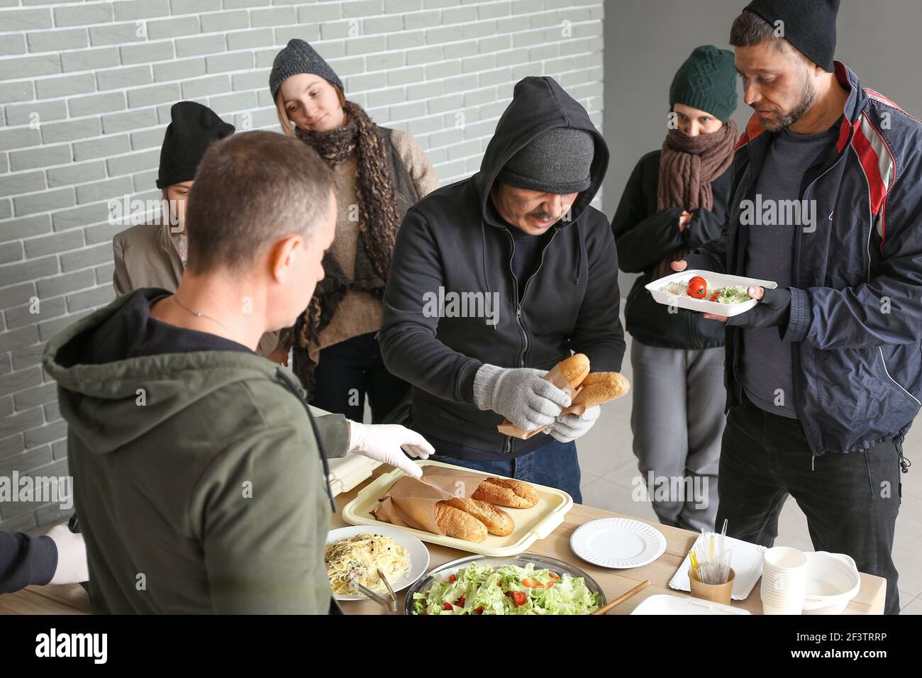 Volunteer giving food to homeless people in warming center Stock Photo