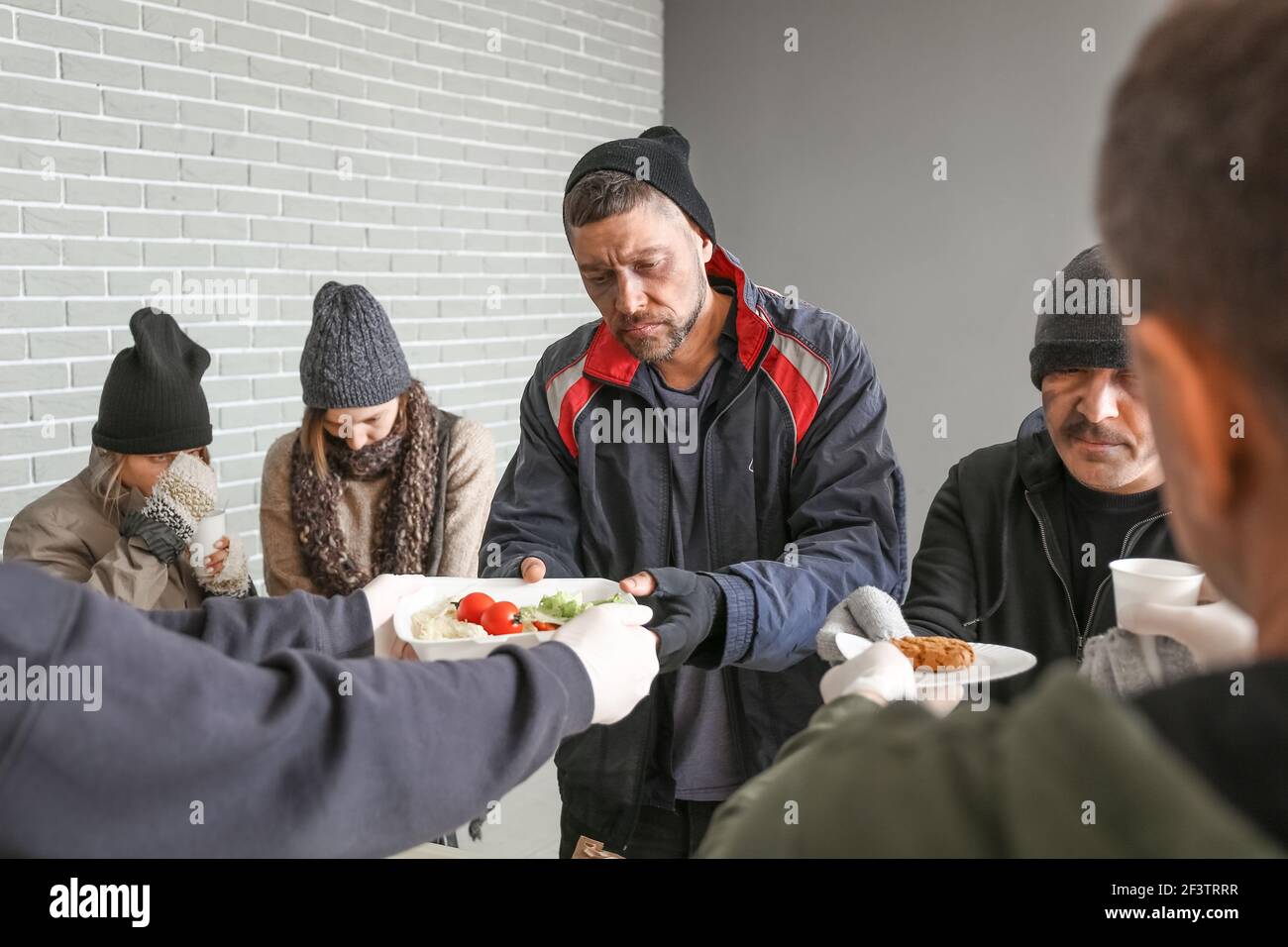 Volunteers giving food to homeless people in warming center Stock Photo