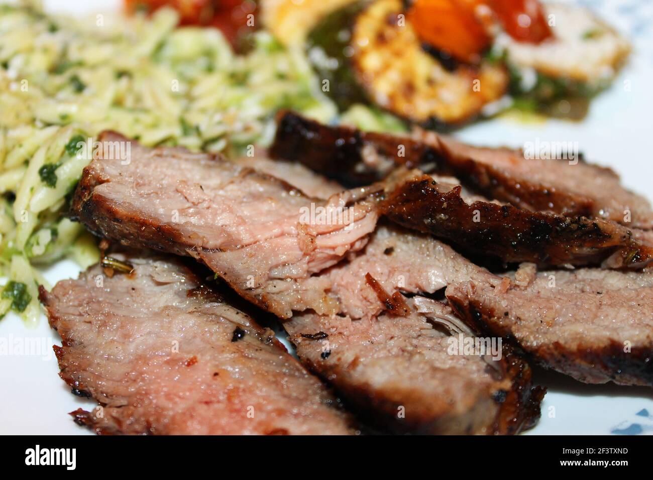 Close-up of sliced baked pork, with basmati rice and fried zucchini and cherry tomatoes out of focus in background. Stock Photo