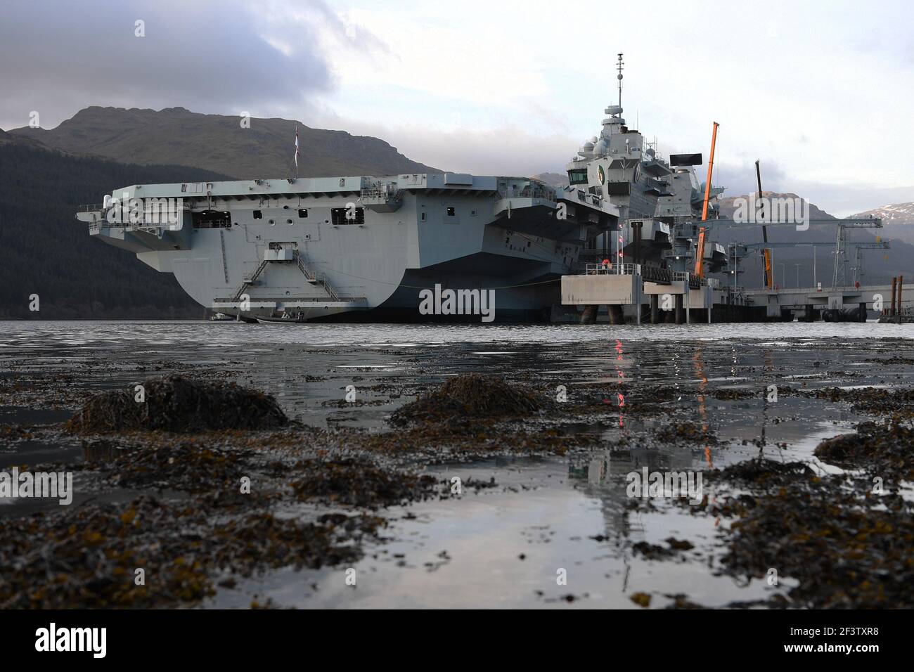 Finnart, Loch Long, Scotland, UK. 17 March 2021.  PICTURED: HMS Queen Elizabeth is the largest and most advanced warships ever built for the Royal Navy. Both HMS Queen Elizabeth (pictured) and HMS Prince of Wales are the nation's flagships which weigh in a 65,000 tonnes and measure 280 meters in length. The Aircraft Carrier is currently berthed on the side of Long Loch at Glen Mallan taking on fuel, munitions  and other supplies, ahead of naval exercises which are part of the UK Carrier Strike Group 2021. The ship is due to leave on Sunday. Credit: Colin Fisher/Alamy Live News. Stock Photo