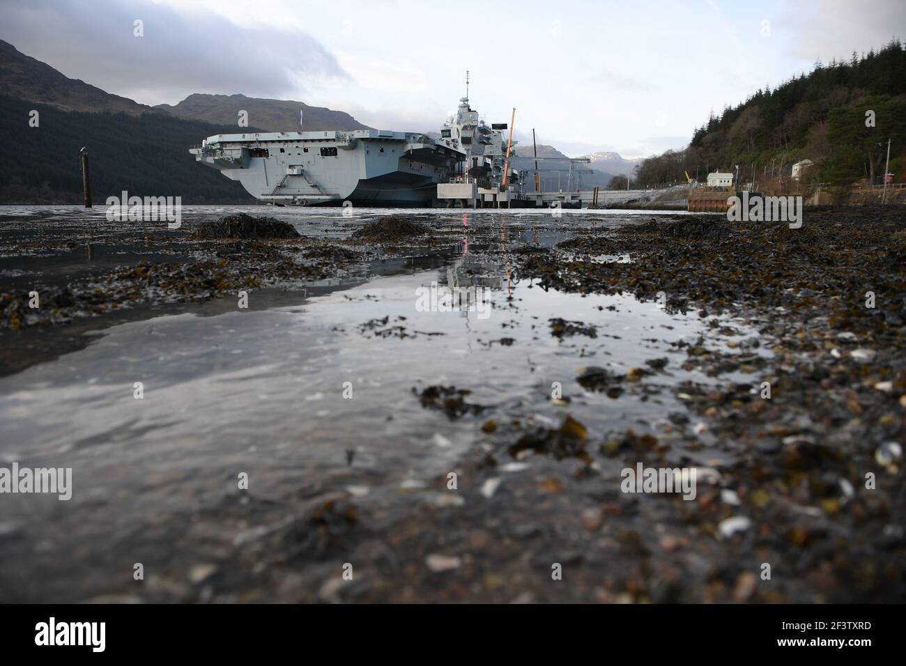 Finnart, Loch Long, Scotland, UK. 17 March 2021.  PICTURED: HMS Queen Elizabeth is the largest and most advanced warships ever built for the Royal Navy. Both HMS Queen Elizabeth (pictured) and HMS Prince of Wales are the nation's flagships which weigh in a 65,000 tonnes and measure 280 meters in length. The Aircraft Carrier is currently berthed on the side of Long Loch at Glen Mallan taking on fuel, munitions  and other supplies, ahead of naval exercises which are part of the UK Carrier Strike Group 2021. The ship is due to leave on Sunday. Credit: Colin Fisher/Alamy Live News. Stock Photo
