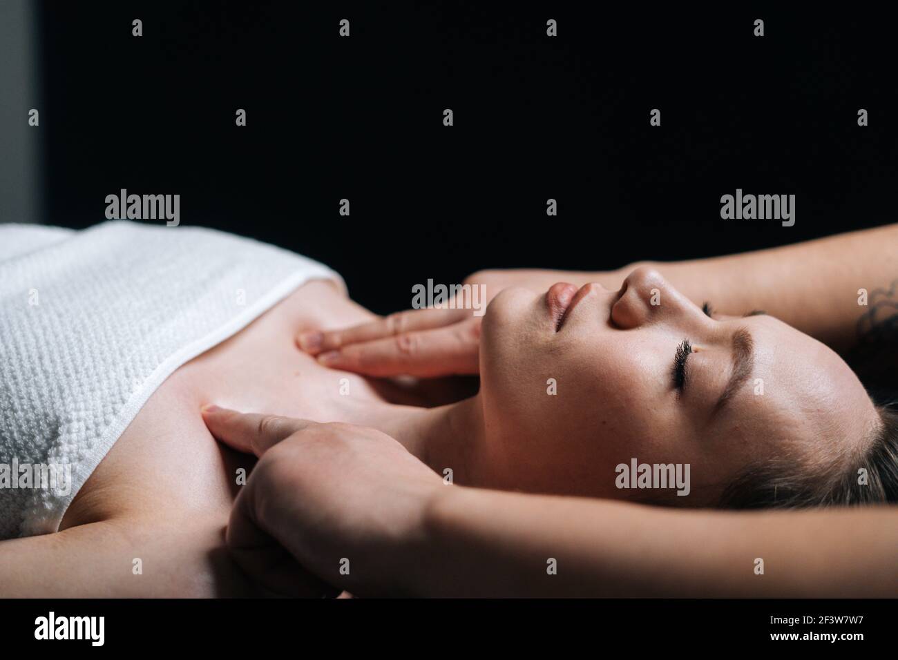 Close-up side view of young woman lying down on massage table during shoulder and neck massage Stock Photo