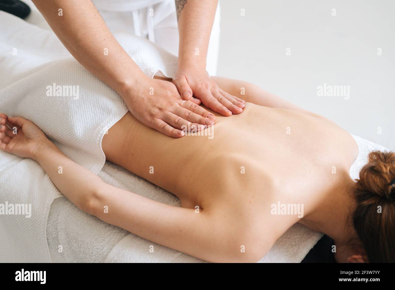 Top view of male masseur massaging back of young unrecognizable woman lying on massage table. Stock Photo