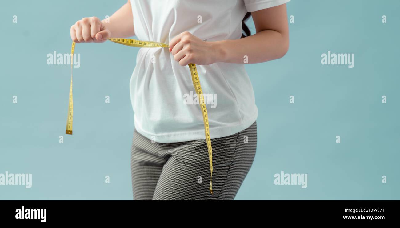 Weight loss, slim body, healthy lifestyle concept. Fit fitness girl measuring her waistline with measure tape on blue Stock Photo