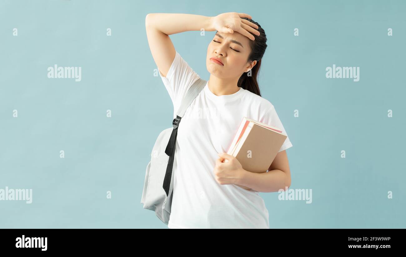 Tired young asian female student in casual clothes backpack hold books put hand on forehead have headache isolated on blue background Stock Photo