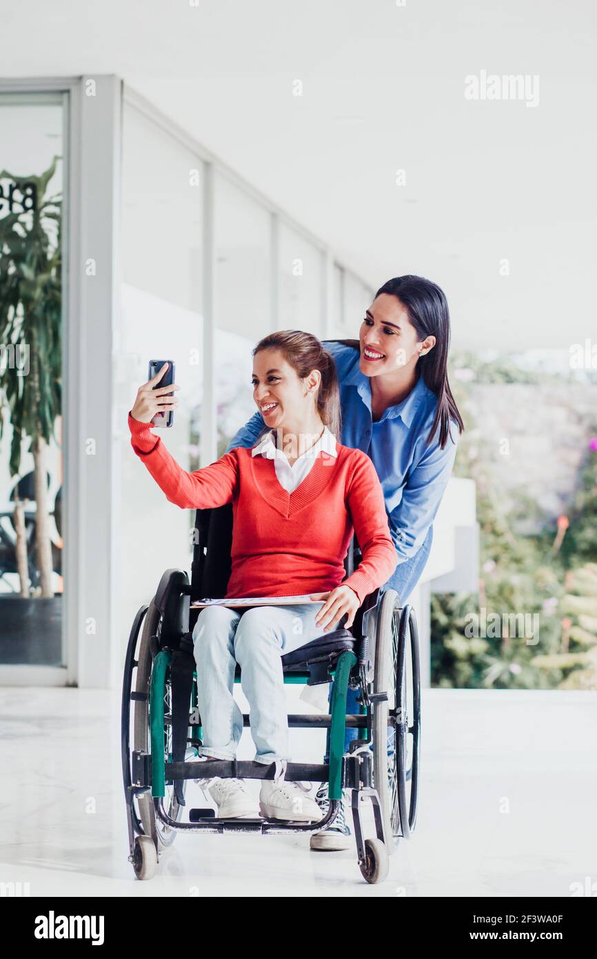 Young latin woman in wheelchair taking a selfie photo at workplace with ...