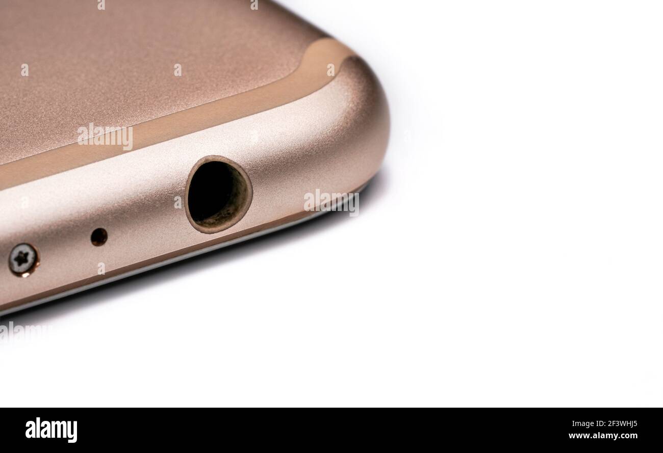Closeup detail of 3.5mm audio jack connector hole on bottom of rose gold coloured mobile phone, isolated white background Stock Photo