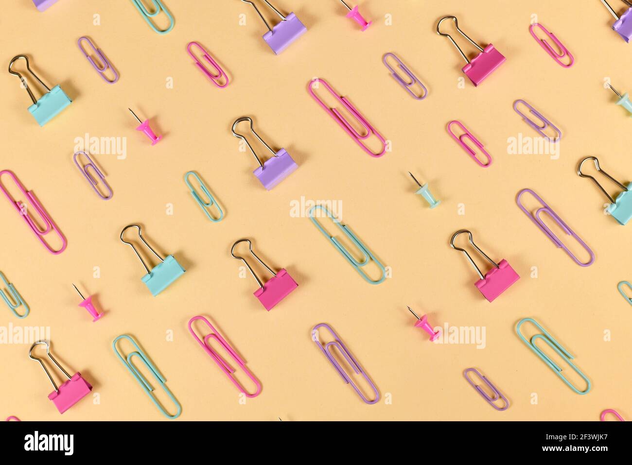 Stationery items like paper clips and drawing pins arranged on side of yellow background Stock Photo