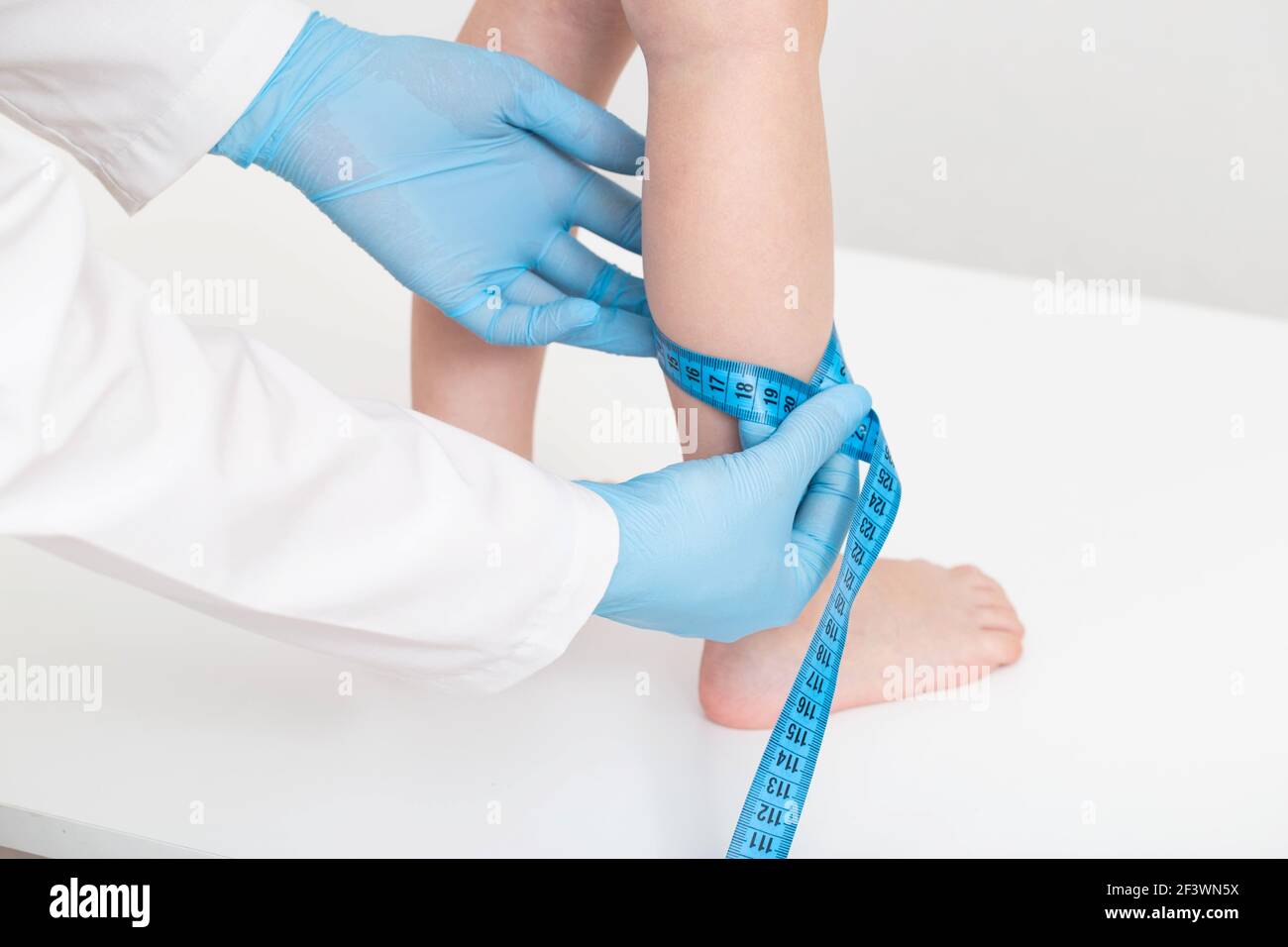 The doctor measures the thickness of the legs of a girl 4 years old with a measuring tape on a white background. The concept of proper nutrition and m Stock Photo