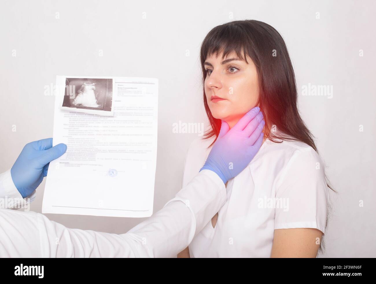 The doctor holds the results of an ultrasound examination of the throat against the background of a female patient who has a pain and a lump in her th Stock Photo
