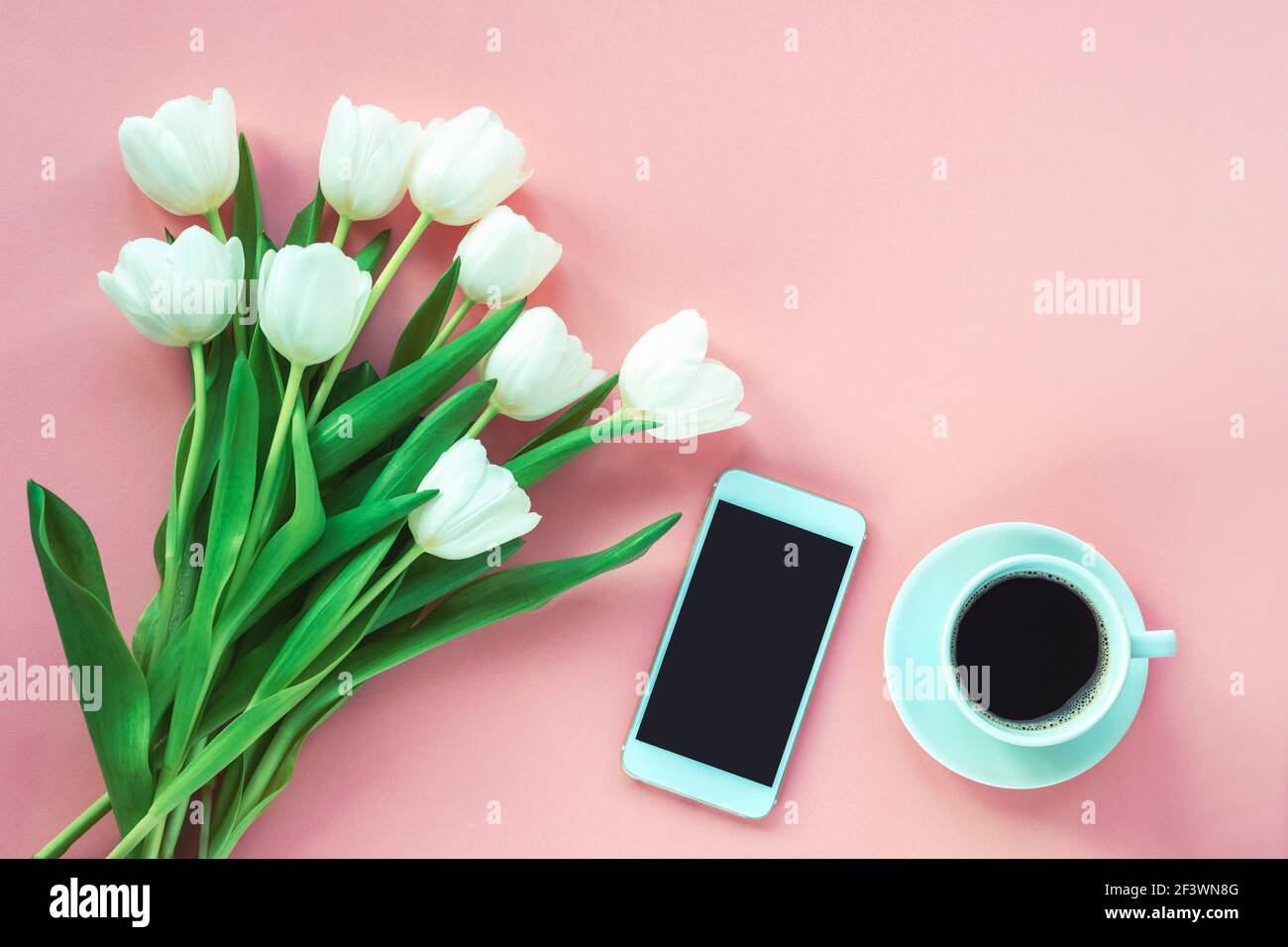 Cup of coffee, smartphone and white tulips on pink background, top view. Women's day or Mother's day concept. Flat lay, copy space. Stock Photo