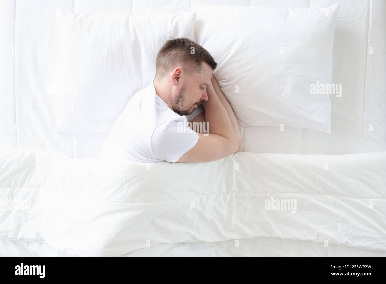 Young man is sleeping peacefully on large white bed Stock Photo
