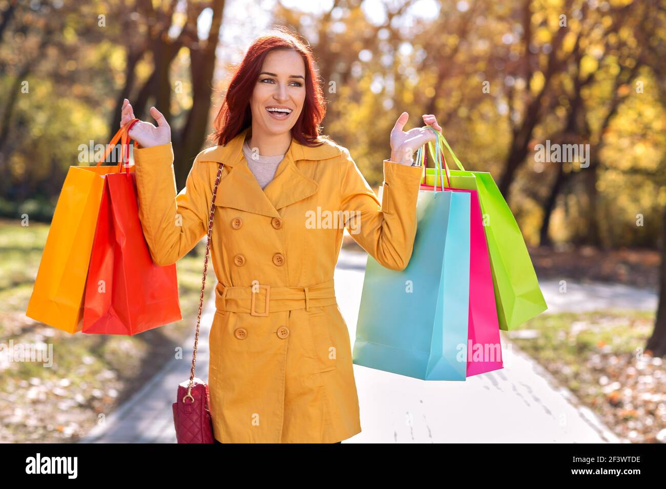 Happy woman in yellow coat holding shopping bags, autumn shopping sale ...