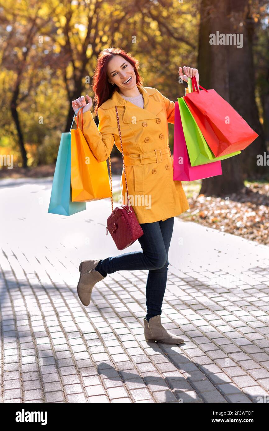 Smiling girl in yellow coat with shopping bags Stock Photo - Alamy