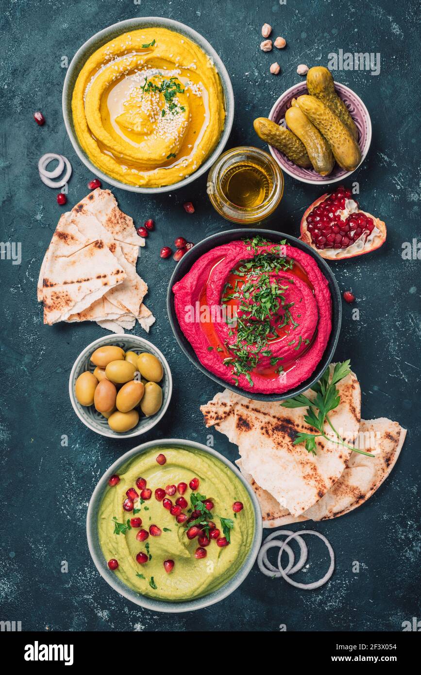 Colorful hummus bowls - green, yellow and beetroot hummus on dark ...
