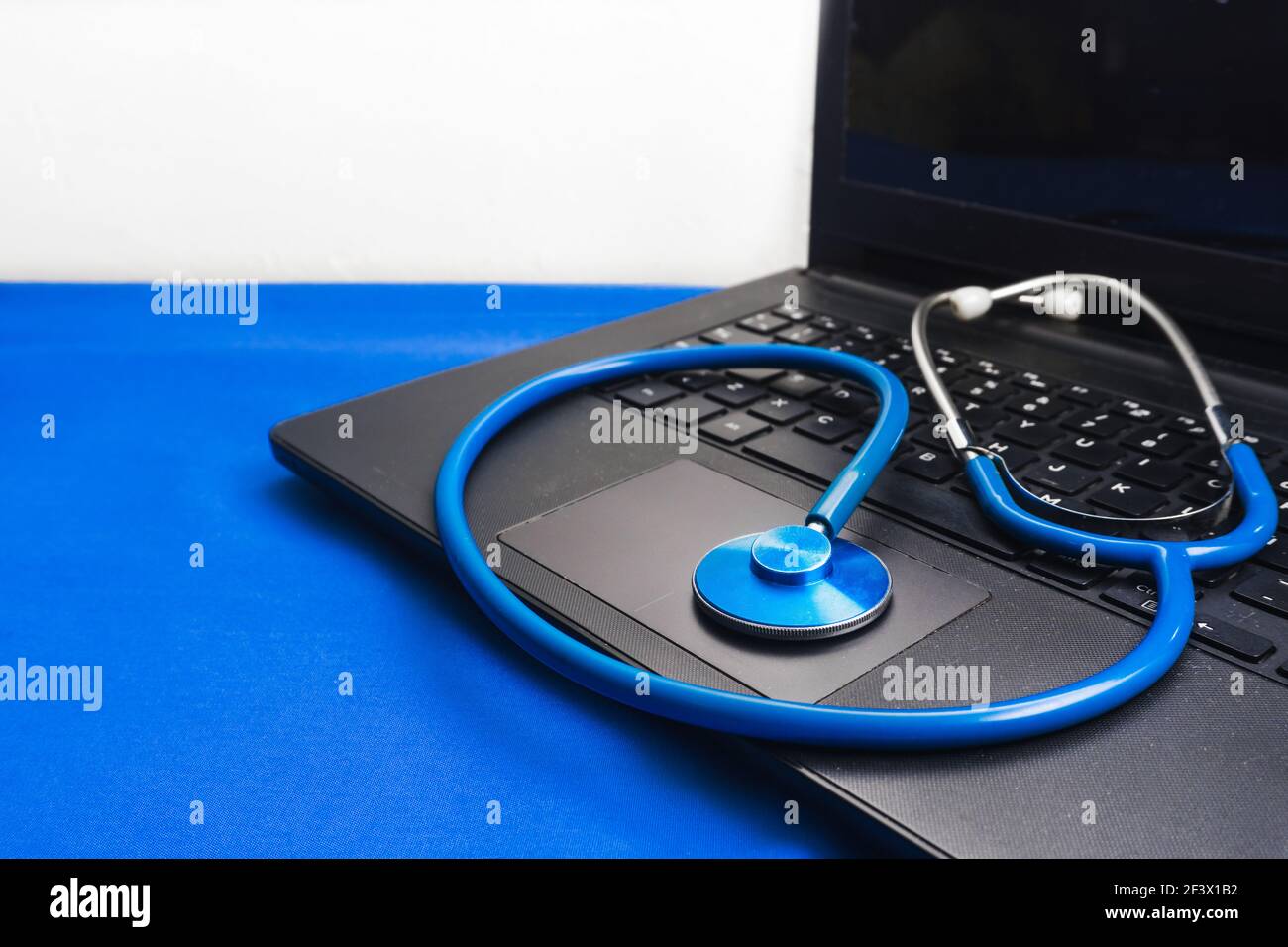 A closeup of a stethoscope on a black laptop on the blue surface Stock Photo