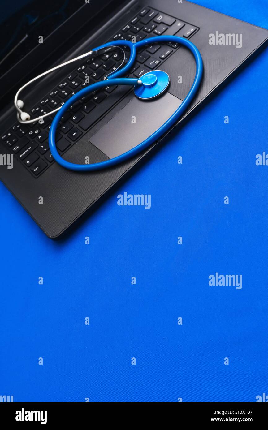 A closeup of a stethoscope on a black laptop on the blue surface Stock Photo