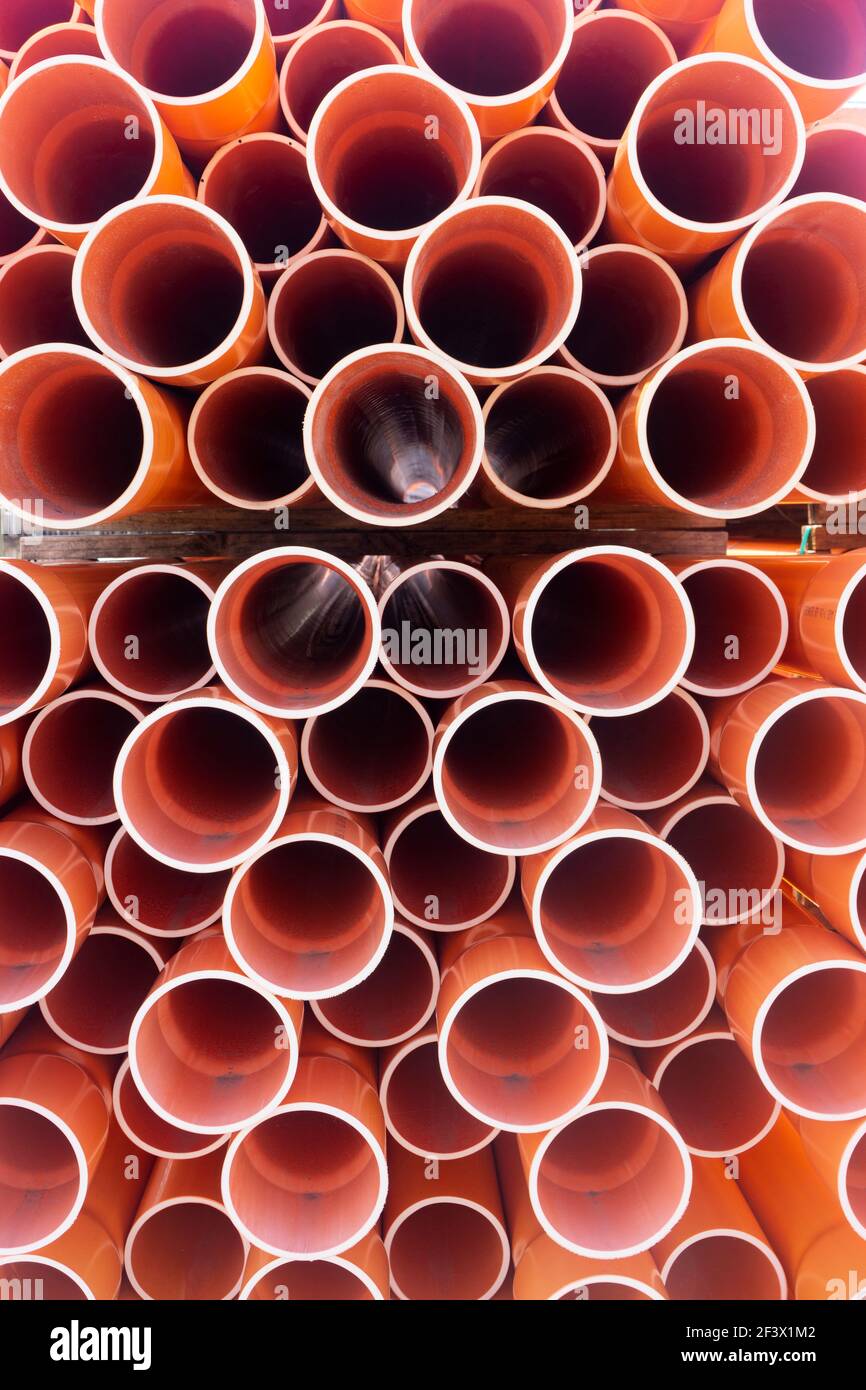 A stack of orange electrical PVC conduit pipes in rows end on in a warehouse giving a repeat pattern of circles. Stock Photo