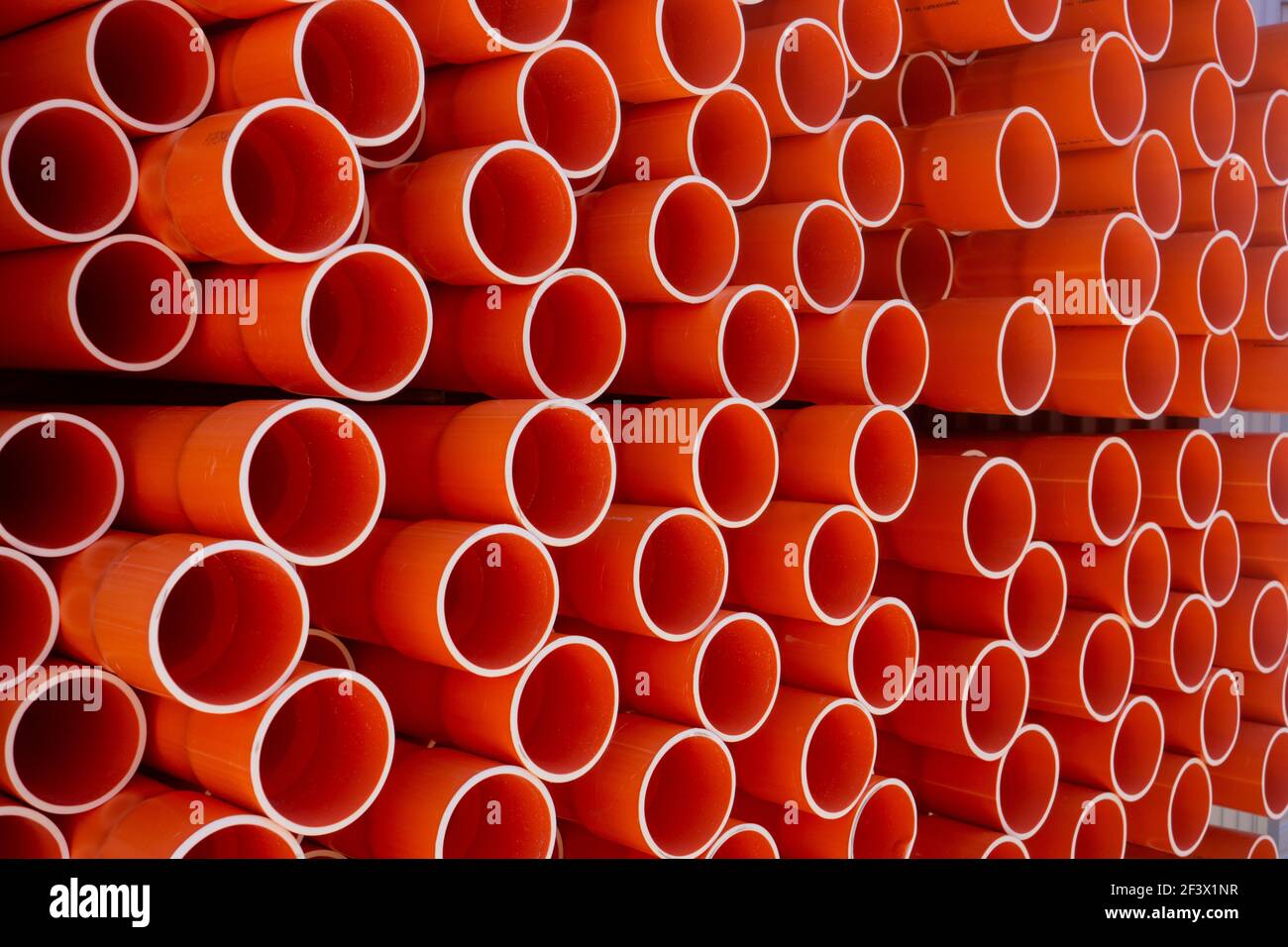 A stack of orange electrical PVC conduit pipes in rows in a warehouse end on giving repeat patterns of circles. Stock Photo