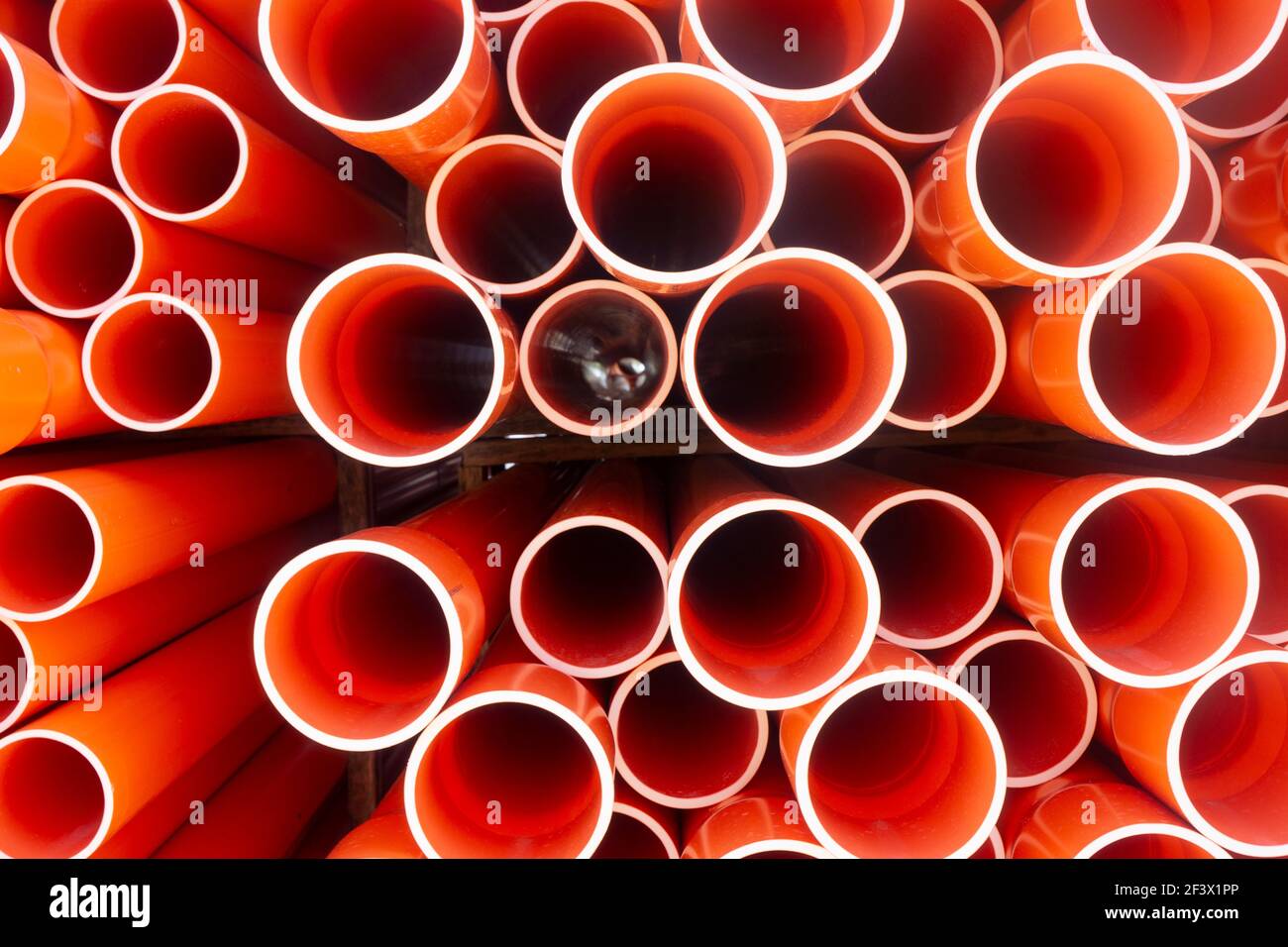 A stack of orange electrical PVC conduit pipes in rows in a warehouse end on giving a repeat pattern of circles. Stock Photo