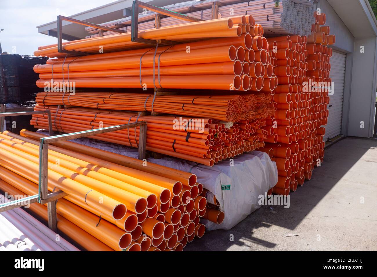 Stacks of orange, yellow and white PVC electrical conduit pipes at a warehouse yard. Stock Photo