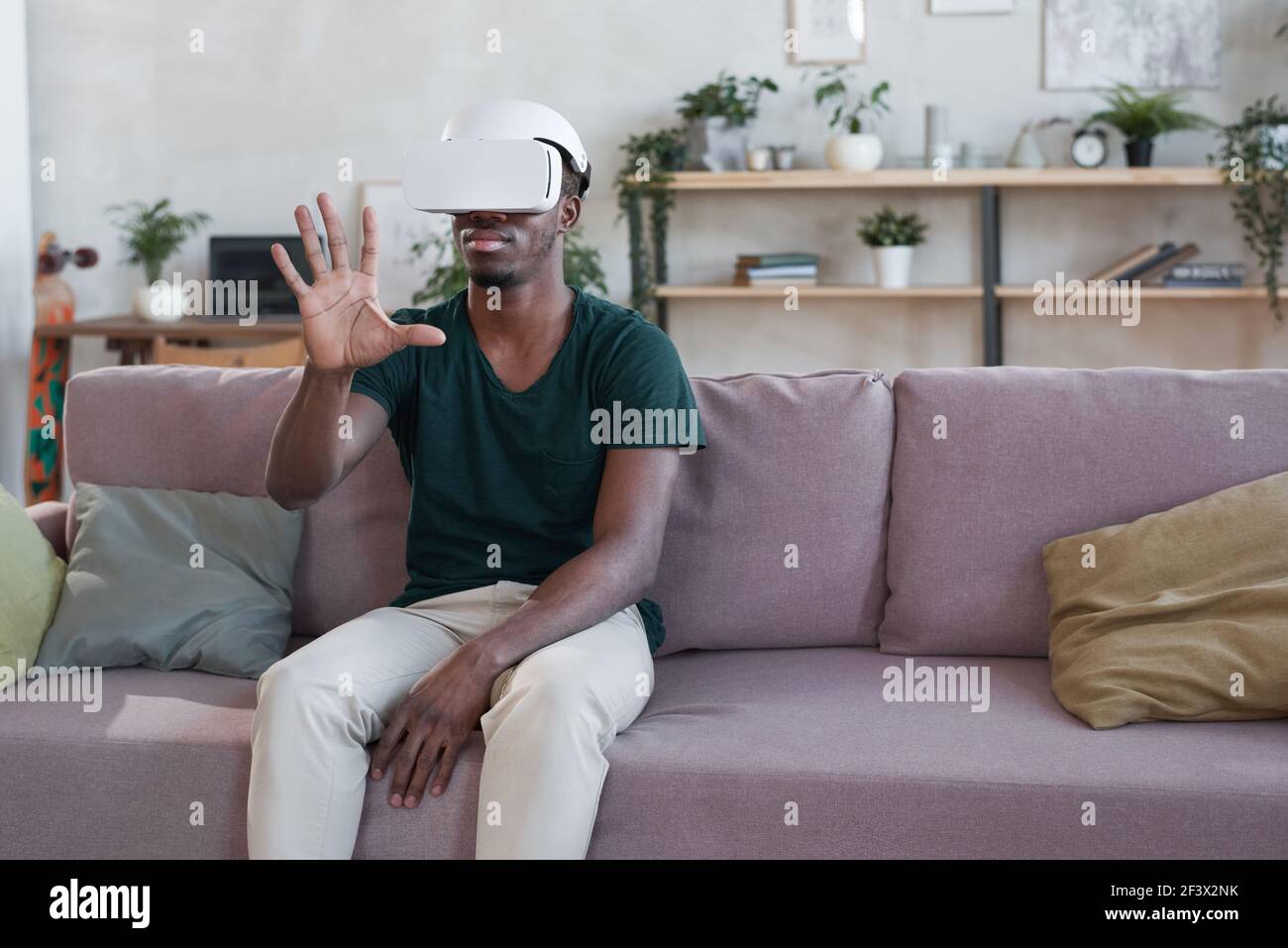 Young African man using VR goggles at home he sitting on sofa and gesturing Stock Photo