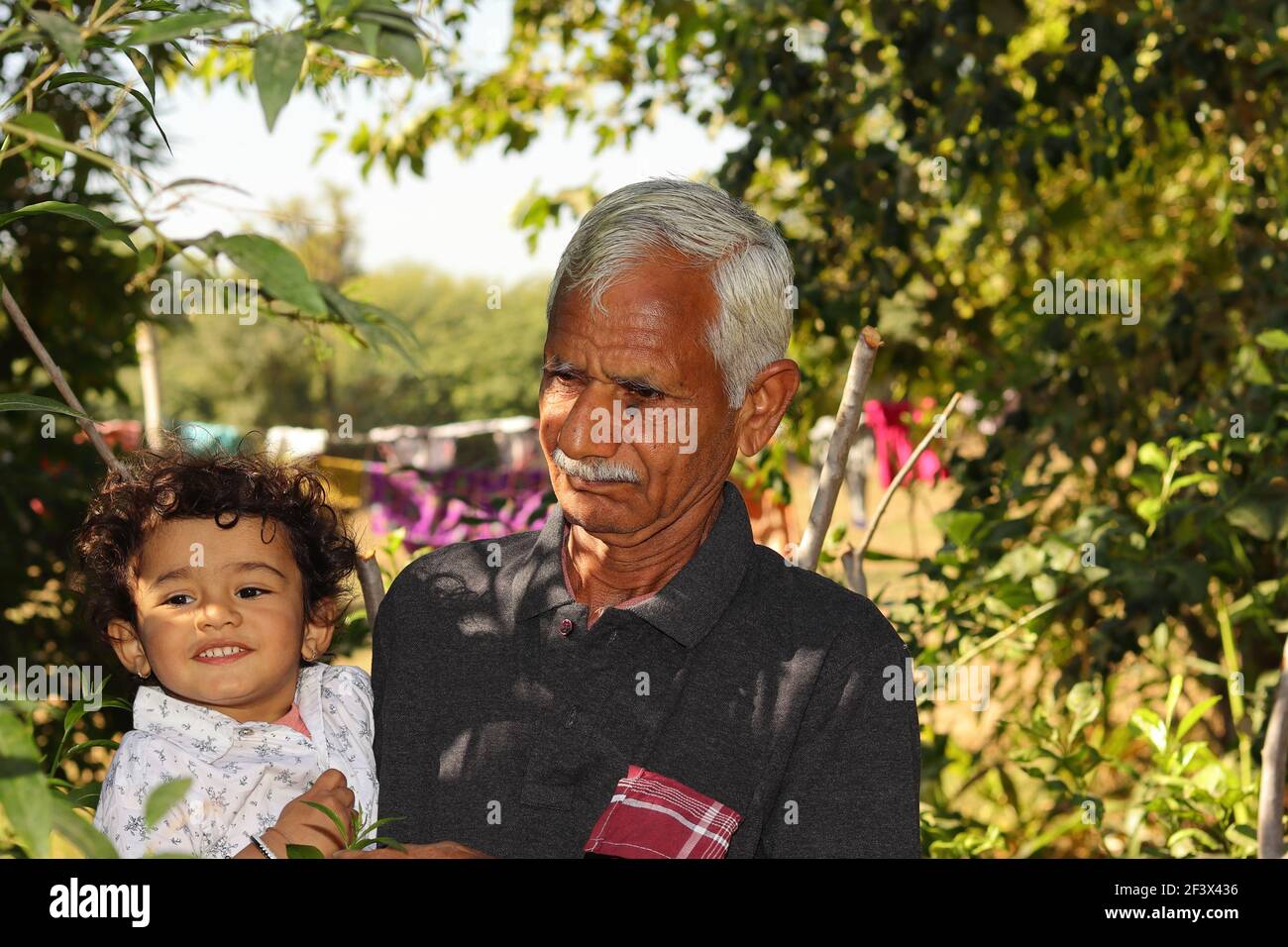 Portrait photo of an indian senior happy grandparents and small grandchildren stand in the garden with smiles, India Stock Photo