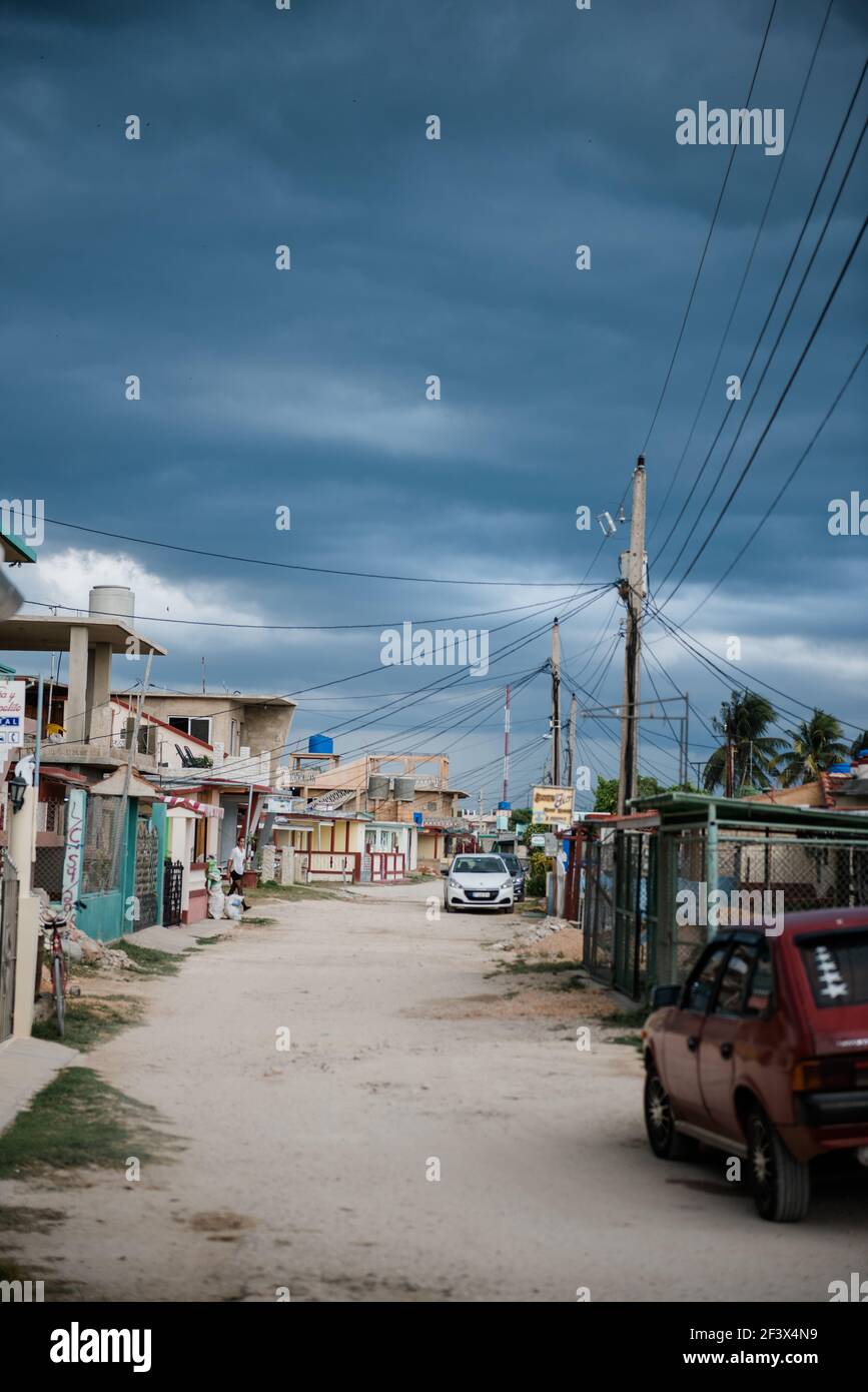 Street in Cuba at Playa Giron, cloudy sky, white sand, power supply line and houses Stock Photo