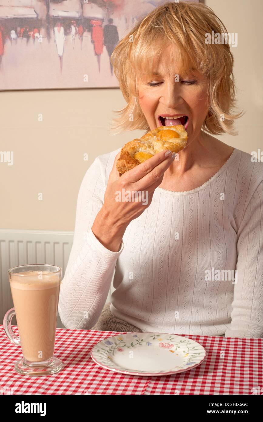 Woman enjoying Danish pastry and latte coffee Stock Photo