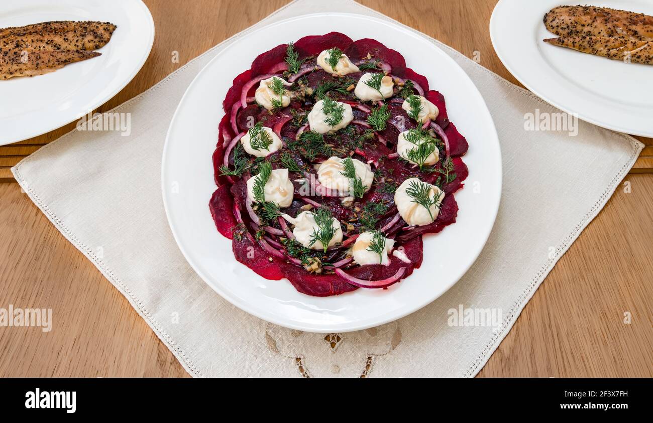 Beetroot salad served on white platter with red onions, dilll and yoghurt with peppered smoked mackerel on dinner plates Stock Photo