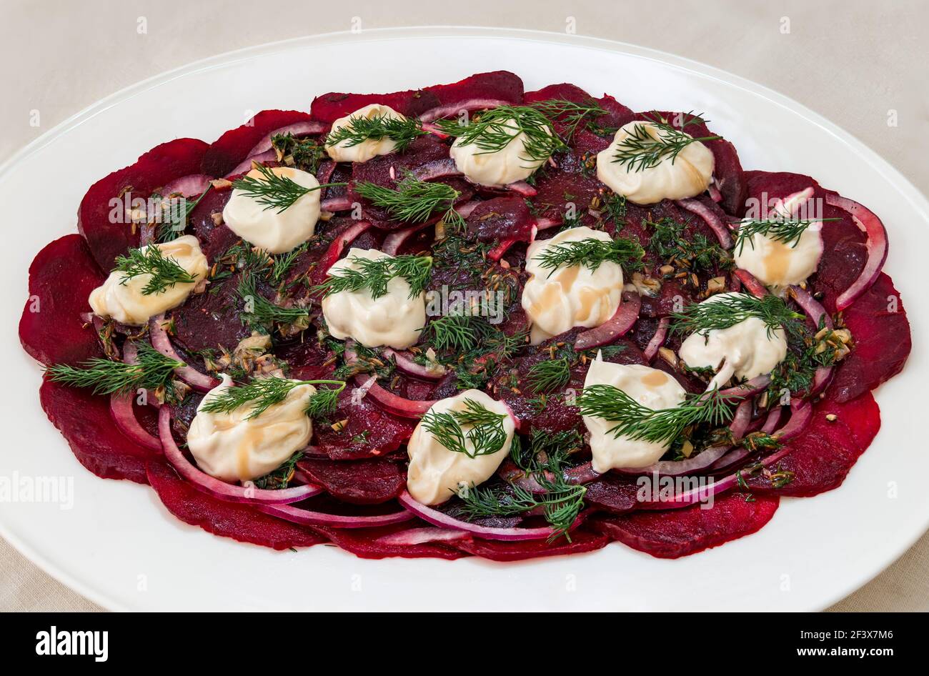 Close up of beetroot salad served on white platter with red onions, dilll and yoghurt with tahini Stock Photo