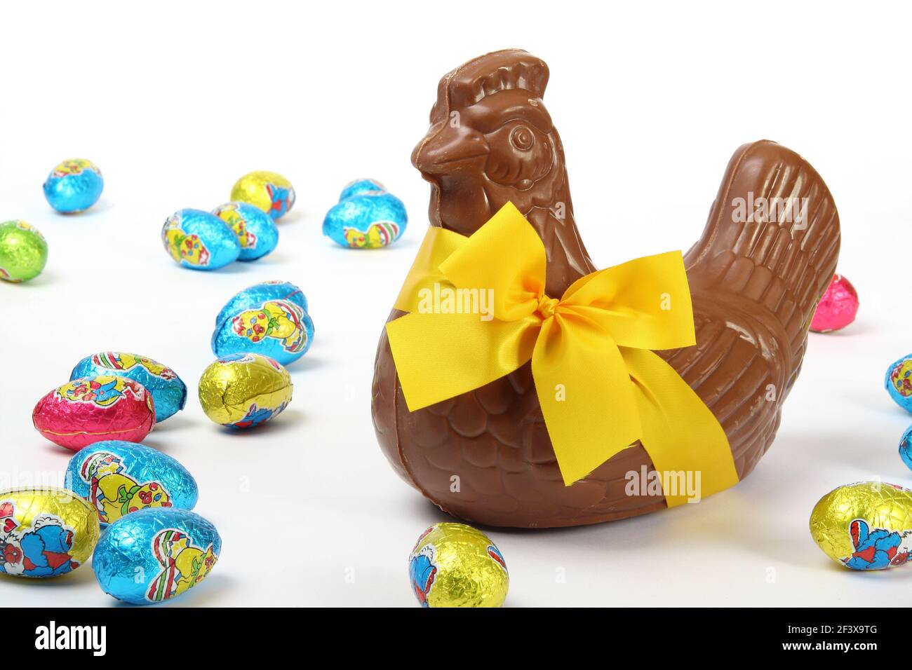 Chocolate Easter hen with yellow ribbon and bow, presented with colorful decorative eggs, isolated on white background - Stock Image