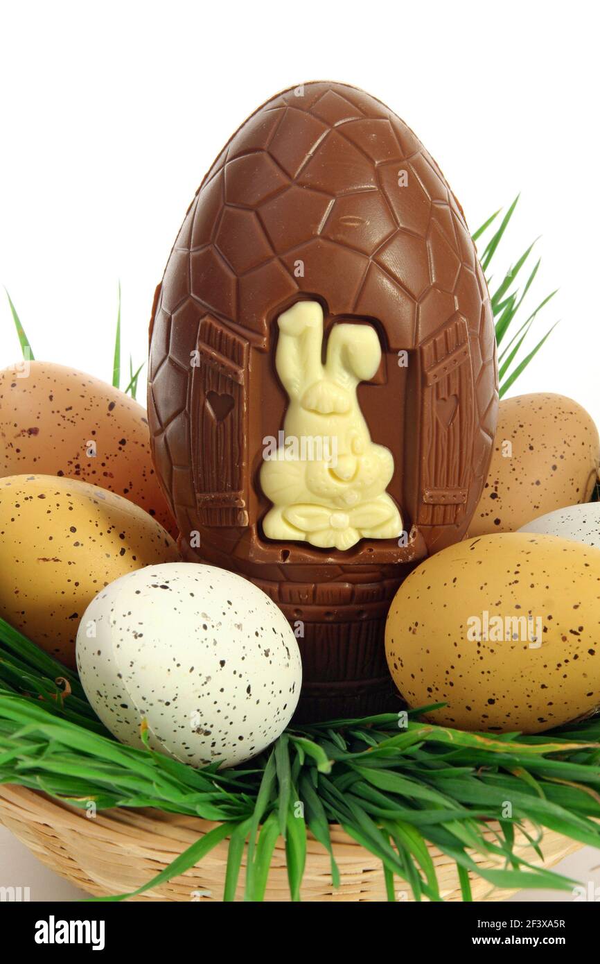 Traditional basket of Easter eggs on fresh grass with a large chocolate egg and a white rabbit - Stock Image