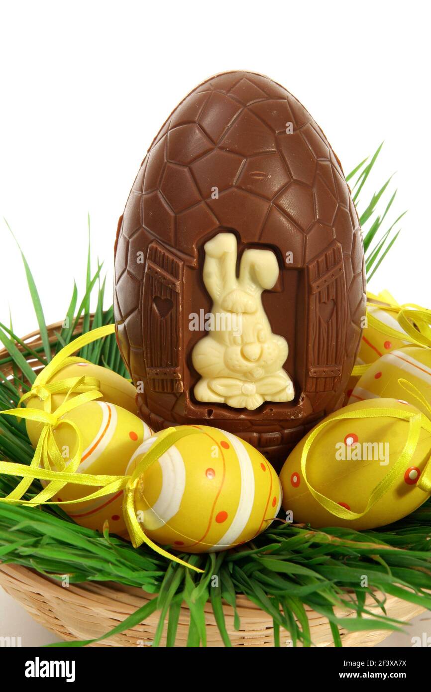 Basket of yellow Easter eggs laid on fresh grass with a large chocolate egg, preparation for the spring celebrations - Stock Image