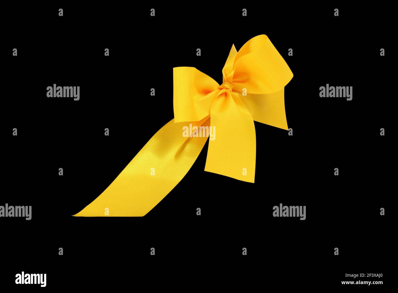 Decorative yellow ribbon and bow cut out and isolated on black background - Stock Image